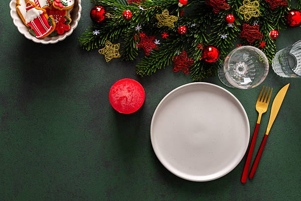 istock A Christmas table setting featuring an empty plate, napkin and gingerbread ,cutlery and a candle on a deep green background. Spruse branches and red tree decorations create a festive atmosphere 2240312818