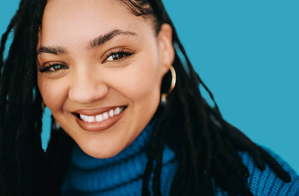 istock Smiling young Black woman with dreadlocks wearing a blue sweater on bright blue background 2240316551