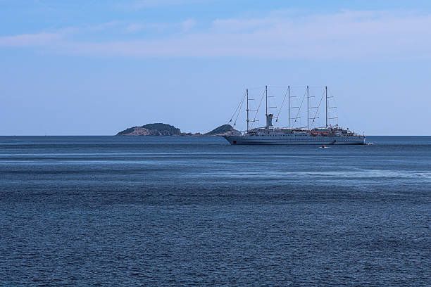 A luxurious cruise ship rests peacefully on the calm blue sea with distant islands in the background. The tranquil ocean and soft hues of the sky create a serene maritime scene that captures the beauty of open-water travel and coastal exploration.