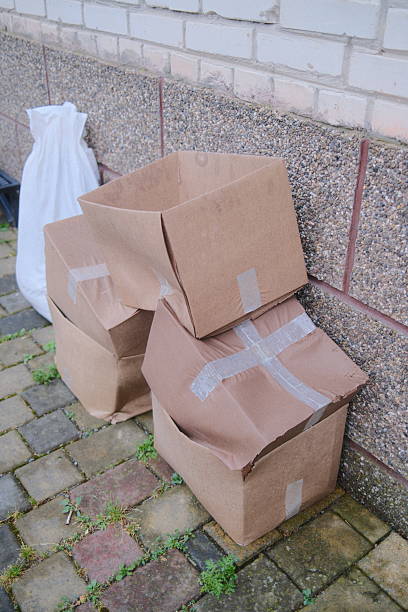 istock Discarded wet cardboard boxes are stacked on a brick path next to a textured wall 2240321777