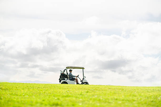 istock Man driving a golf cart across green fairway under cloudy sky. 2240326046