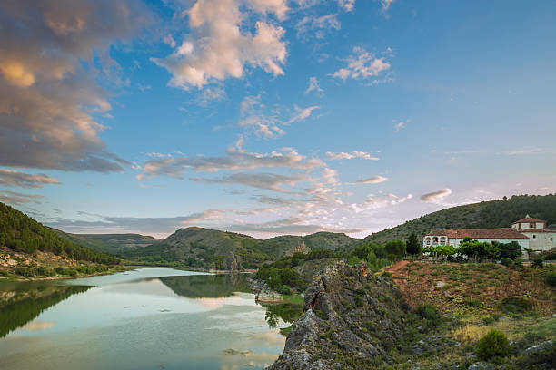 A landscape between mountains on the shore of a lake with a farmhouse on one side