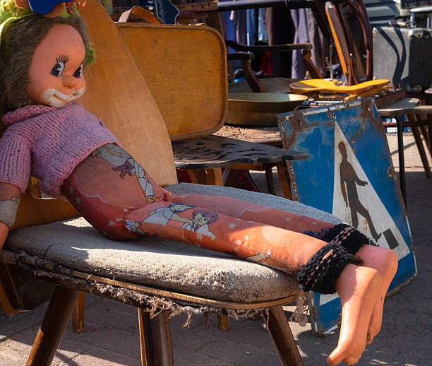 A vintage doll with a cracked body and faded clothes resting on an old chair at a flea market. The image symbolizes nostalgia, decay, and the passage of time.
