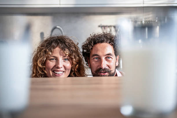 Happy couple peeking over kitchen counter looking at camera