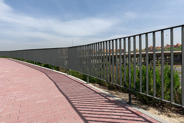 istock Brick pathway with metal railing casting shadow over them in an urban park 2240335605