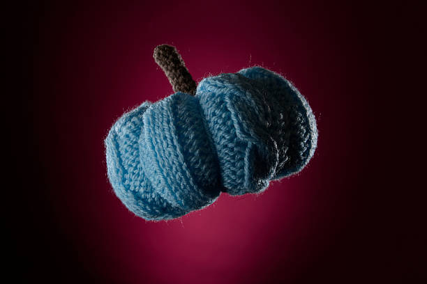 Studio photo of blue knitted pumpkin with visible texture on a dark magenta background. Represents autumn, harvest, cozy home and handmade creativity. Perfect for seasonal craft design concepts.