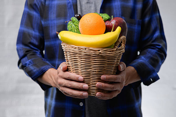 Man Holding a Basket of Fresh Fruits on a Light Background