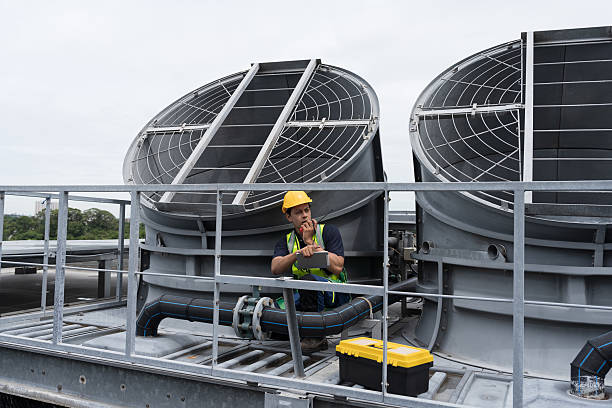 istock Cooling tower on rooftop. Induced draft cooling tower. Male engineer or technician maintenance and repair of cooling tower on rooftop of building, wearing safety uniform, helmet, using handyman tools 2240380079