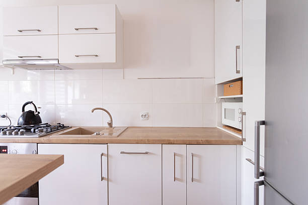 A sleek and contemporary kitchen that beautifully showcases striking white cabinetry accompanied by a wooden countertop