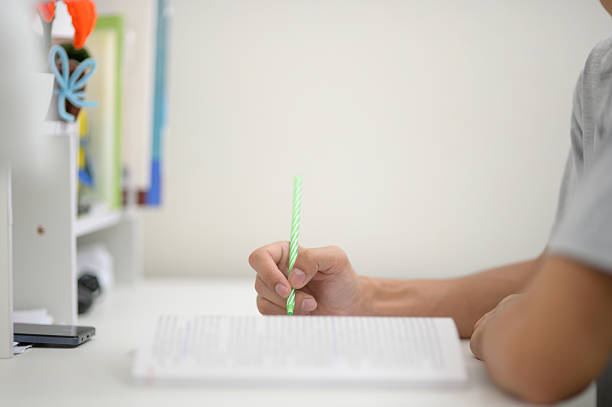 A close-up of a focused hand writing notes in a notebook using a green straw pen on a clean desk, showcasing a minimalist workspace ideal for studying or planning.