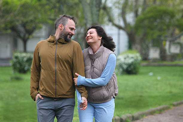Happy middle-aged couple walking together outdoors in spring or autumn, enjoying nature and spending time hiking or exploring the park.