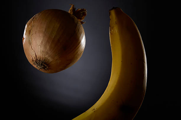 A banana and onion arranged together on a dark background under soft lighting for a creative and contrasting food composition concept with rich shadows and textures.