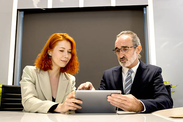 istock Two businesspeople discussing, looking information on tablet at office workplace.  Beautiful businesswoman has discussion together with senior manager. Mature businessman boss working with secretary. 2240406030