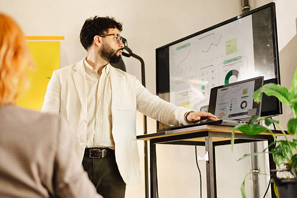 istock Business presentation by a man in a white jacket in a modern office space with visual data on screens during a daytime meeting 2240412900