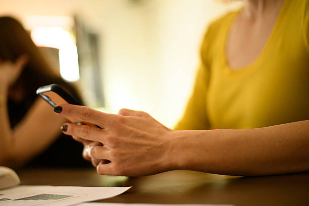 istock Young woman using smartphone while sitting at a table in a bright indoor space engaged with friends or coworkers 2240412943