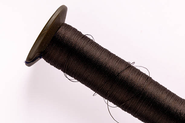 A large, long spool of black thread, macro shot on a white background