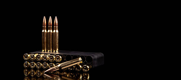 istock Gold bullets in a black ammo box and three standing bullets on a dark, reflective surface. 2240414009