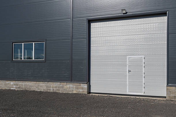 istock A modern warehouse facade with gray walls, white sectional doors, and windows. 2240417747