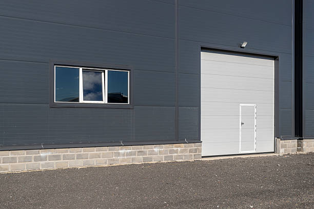 istock A modern warehouse facade with gray walls, white sectional doors, and windows. 2240417752