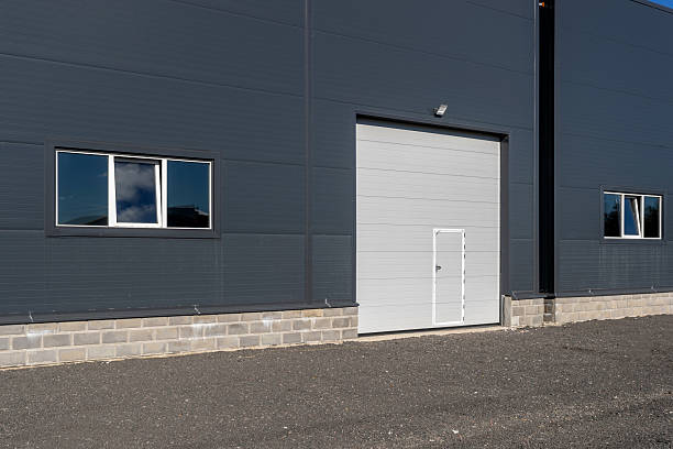 istock A modern warehouse facade with gray walls, white sectional doors, and windows. 2240417766