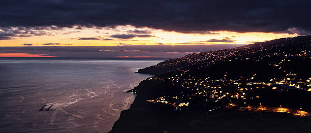 Wide panoramic view of Madeira’s illuminated coastline as night falls, with glowing sky and calm Atlantic waters.