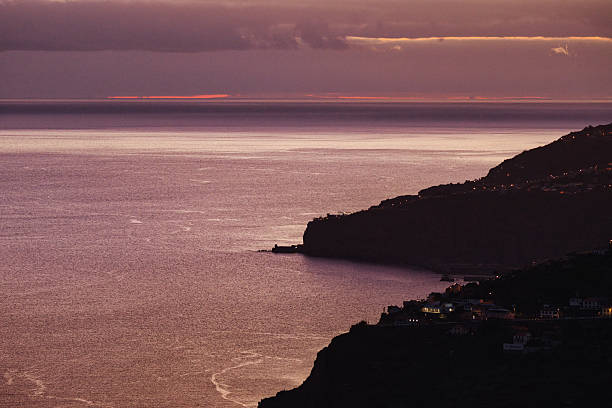 Peaceful view of Madeira island’s cliffs fading into night under purple and orange dusk light over the Atlantic Ocean.