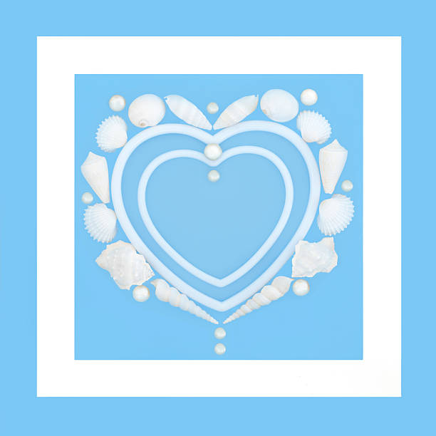 Heart shaped seashell and pearl wreath on blue background with white frame border. Romantic natural symbol of love for Valentines, anniversary or birthday greeting card.