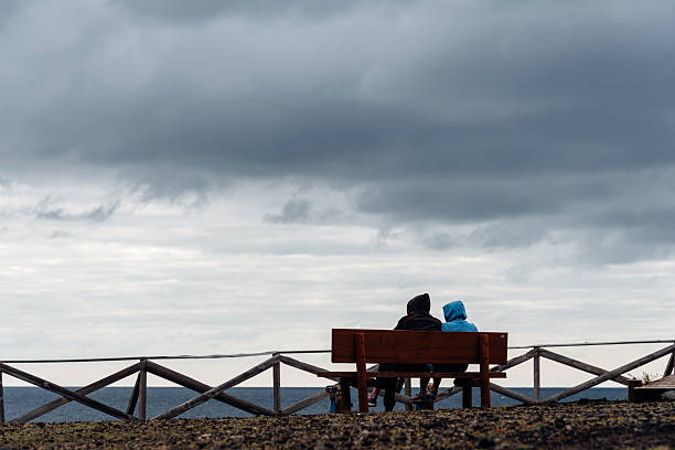 Two people sit on a bench overlooking the ocean under a cloudy sky in Sao Miguel, Azores.