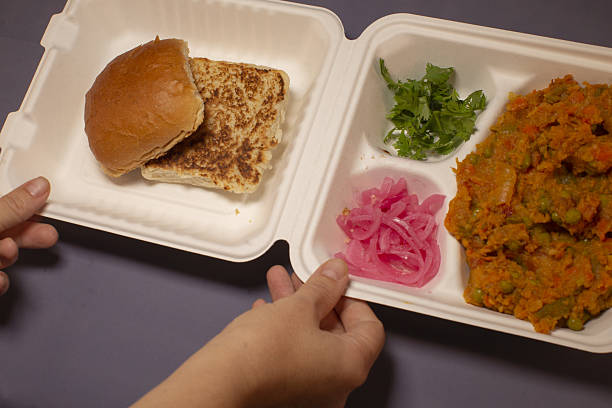 A convenient takeout meal consisting of a delicious sandwich, fresh vegetables, and pickled onions in a container