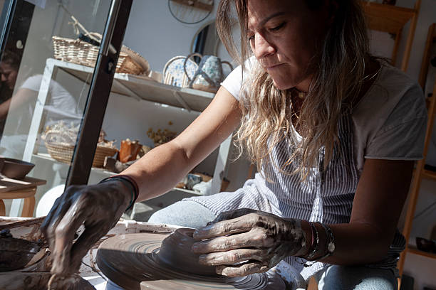 istock Focused woman shaping clay on spinning pottery wheel 2240452375