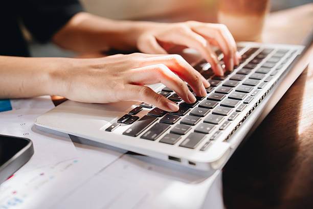 istock Typing concept. Hands Typing on Laptop Keyboard with Papers and Smartphone on Table in Bright Natural Light 2240459950