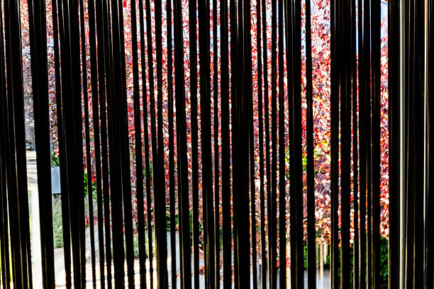 Metal rods attached to a floor stand create a movable wind screen that allows for visibility. Beside large sliding glass window that looks into a courtyard with trees and plants.  Sways in the wind and can make noise.