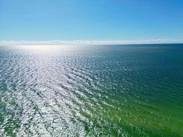 Aerial view of a vast ocean under a clear blue sky with sunlight reflecting on the water.