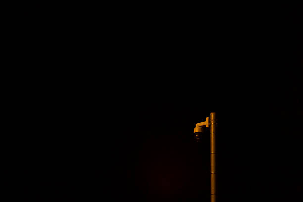 A tall pole equipped with camera stands firmly against a dark, background during the night