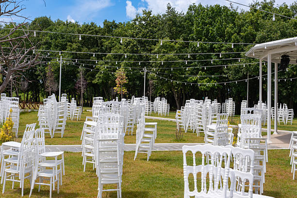 istock White chairs stacked in outdoor garden under string lights and trees. White wedding chairs in grassy area, minimalist green lawn. Event and outdoor celebration concept 2240485716