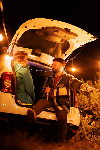 istock Couple enjoying late night conversations by a car trunk under warm string lights in a serene outdoor setting 2240494418