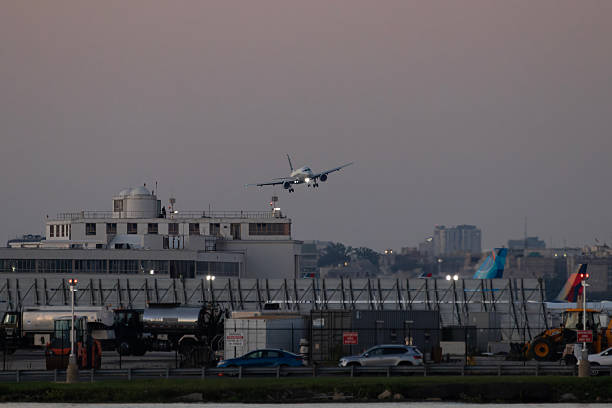 10-03-2025 Arlington, Virginia, USA - An airplane prepares to land at Ronald Reagan Washington National Airport during dusk, with terminal buildings and parked aircraft visible under a pastel evening sky.