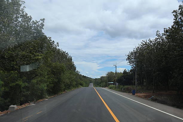 istock An empty road with a white center line running down its length. The road is flanked by trees and appears to be in a rural area, given the sparse vegetation along the side 2240534407