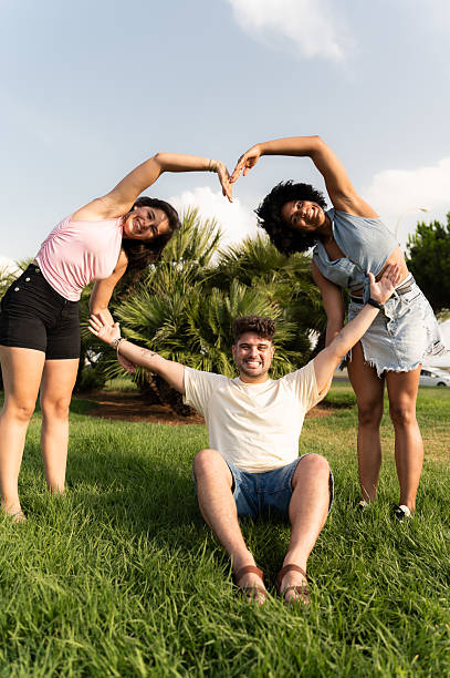 Group of happy young adults forming a heart shape with their hands in a park