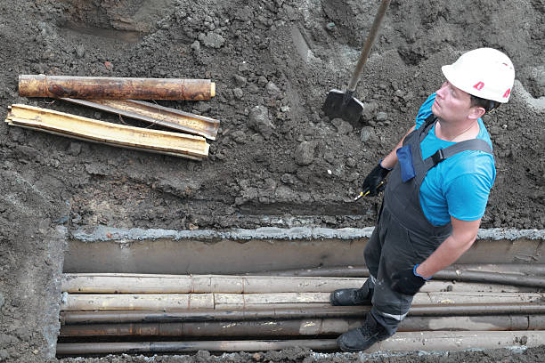 istock Male construction worker in blue uniform standing in trench at worksite 2240538456