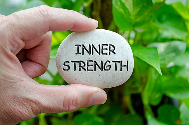 istock Hand holding a white stone with INNER STRENGTH text engraved on it, representing life purpose of resilience and personal power. 2240542976