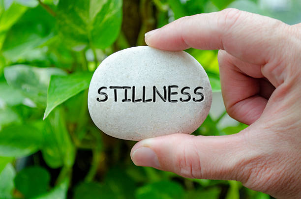 Hand holding a white stone with STILLNESS text engraved on it, representing life purpose of tranquility and peace of mind