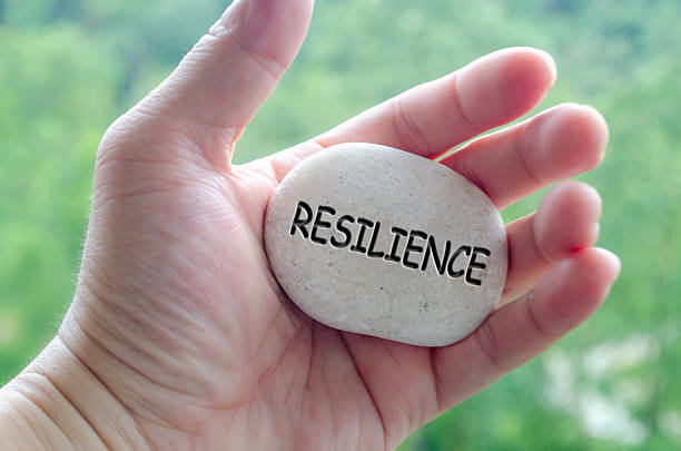 Hand holding a white stone with RESILIENCE text engraved on it, reflecting life purpose of endurance and emotional strength.