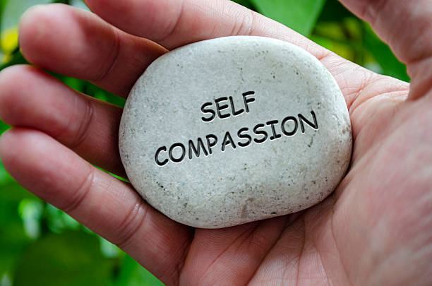 istock Hand holding a white stone with SELF COMPASSION text engraved on it, signifying life purpose of kindness toward oneself and healing. 2240543004