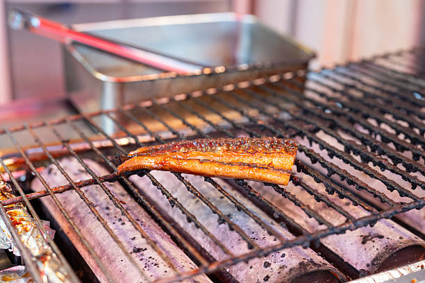 A big piece of eel or unagi is grilling on charcoal flame at the fish market, on of the most famous traditional Japanese food menu. Selective focus.