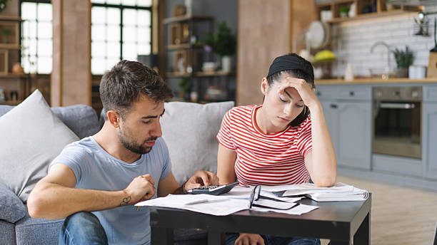 istock Couple calculating bills at home using tablet and calculator. Young couple working on computer while calculating finances sitting on couch. Young man with wife at home analyzing their finance with documents. 2240546578