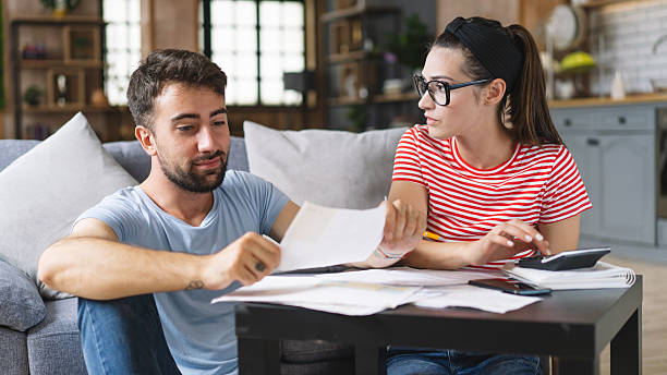 istock Couple calculating bills at home using tablet and calculator. Young couple working on computer while calculating finances sitting on couch. Young man with wife at home analyzing their finance with documents. 2240546582