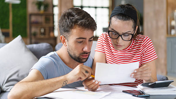 istock Couple calculating bills at home using tablet and calculator. Young couple working on computer while calculating finances sitting on couch. Young man with wife at home analyzing their finance with documents. 2240546585