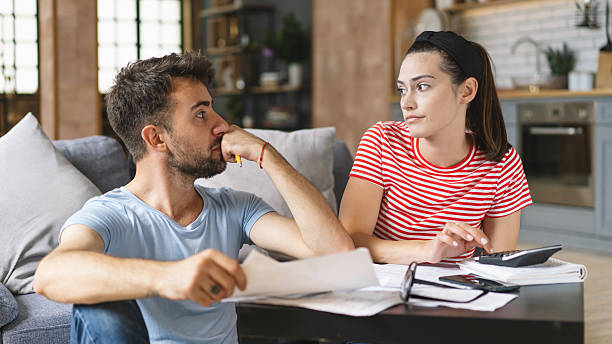 istock Couple calculating bills at home using tablet and calculator. Young couple working on computer while calculating finances sitting on couch. Young man with wife at home analyzing their finance with documents. 2240546586