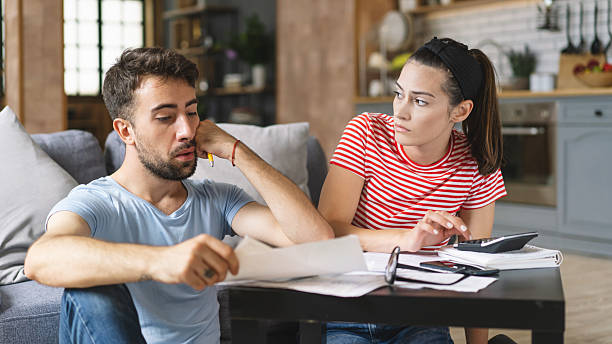 istock Couple calculating bills at home using tablet and calculator. Young couple working on computer while calculating finances sitting on couch. Young man with wife at home analyzing their finance with documents. 2240546588